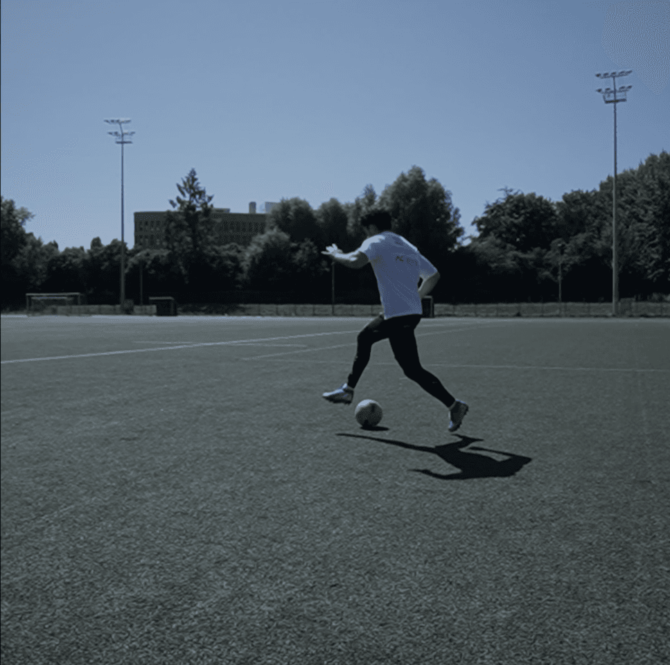 Athlete striking a football on an outdoor pitch while wearing the Skinetix garment during a measurement session.