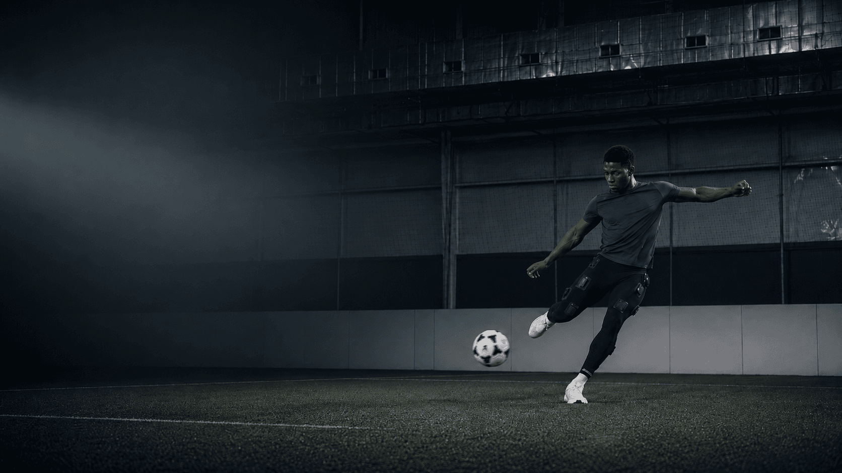Footballer striking a ball on an indoor pitch while wearing the Skinetix sensor-integrated leggings.