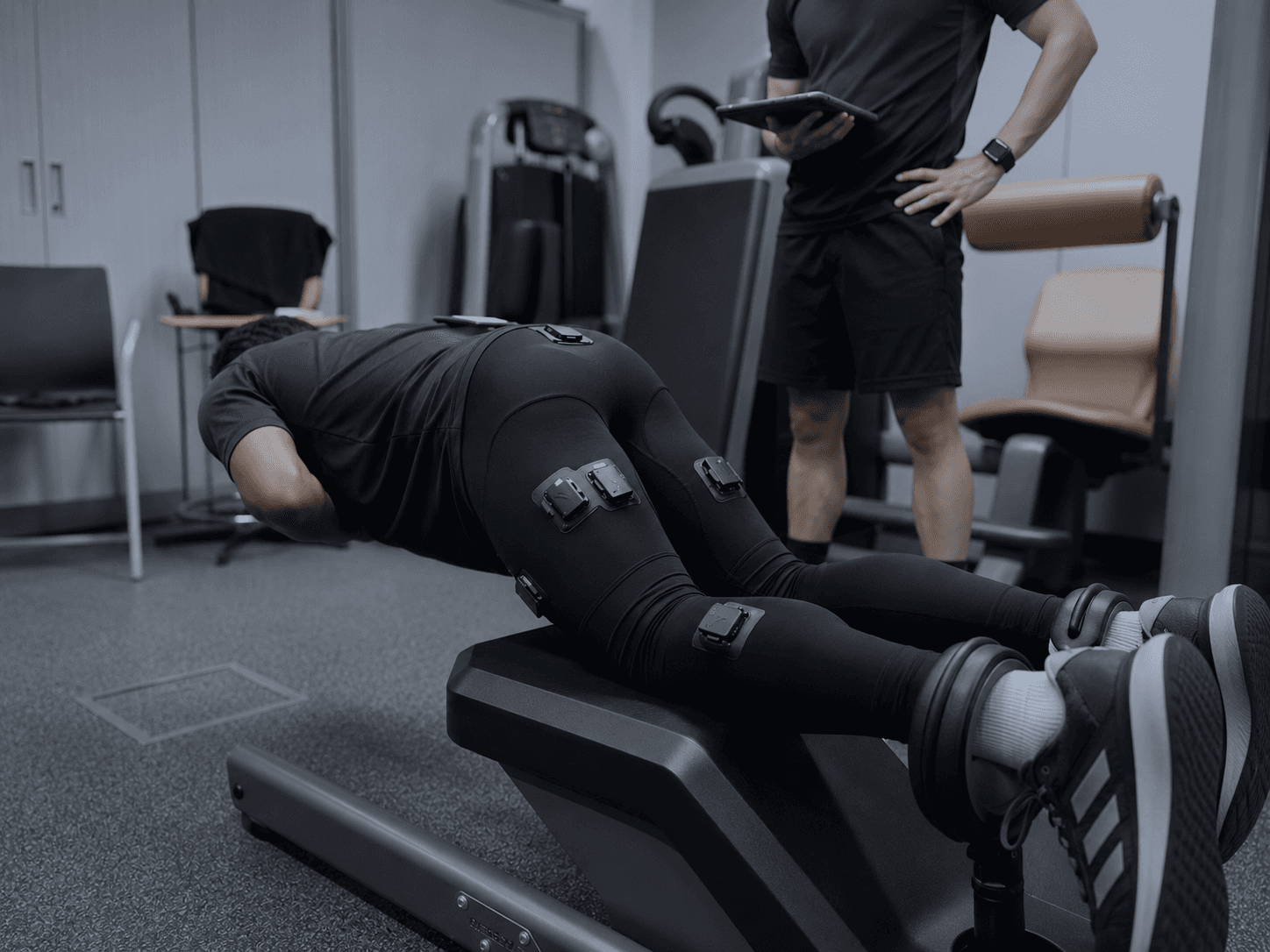 Athlete performing a Nordic hamstring exercise in the Skinetix garment while a practitioner observes with a tablet.
